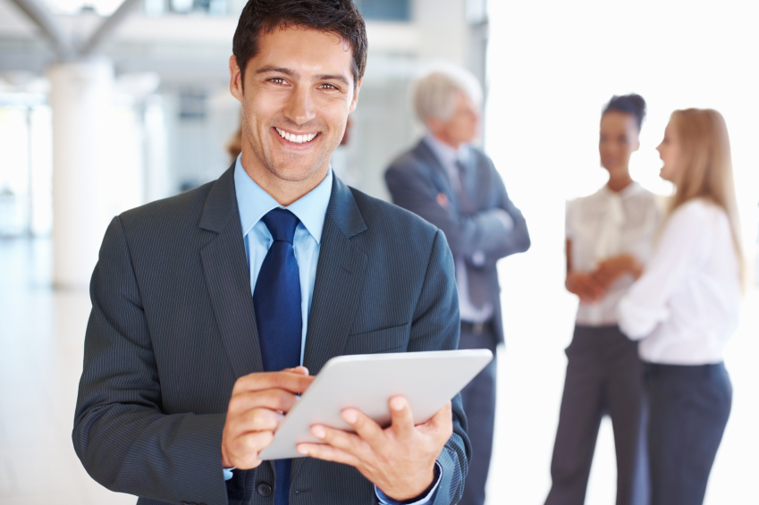 Portrait of smiling young business man working on digital tablet with executives in background